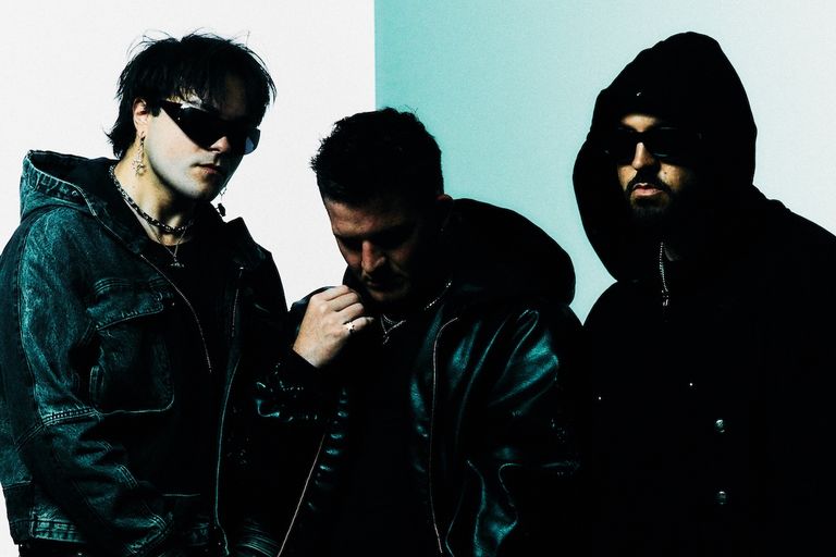 Band members of Banks Arcade pose in dark jackets against a split white and light blue background, two wearing sunglasses and one wearing a hood.